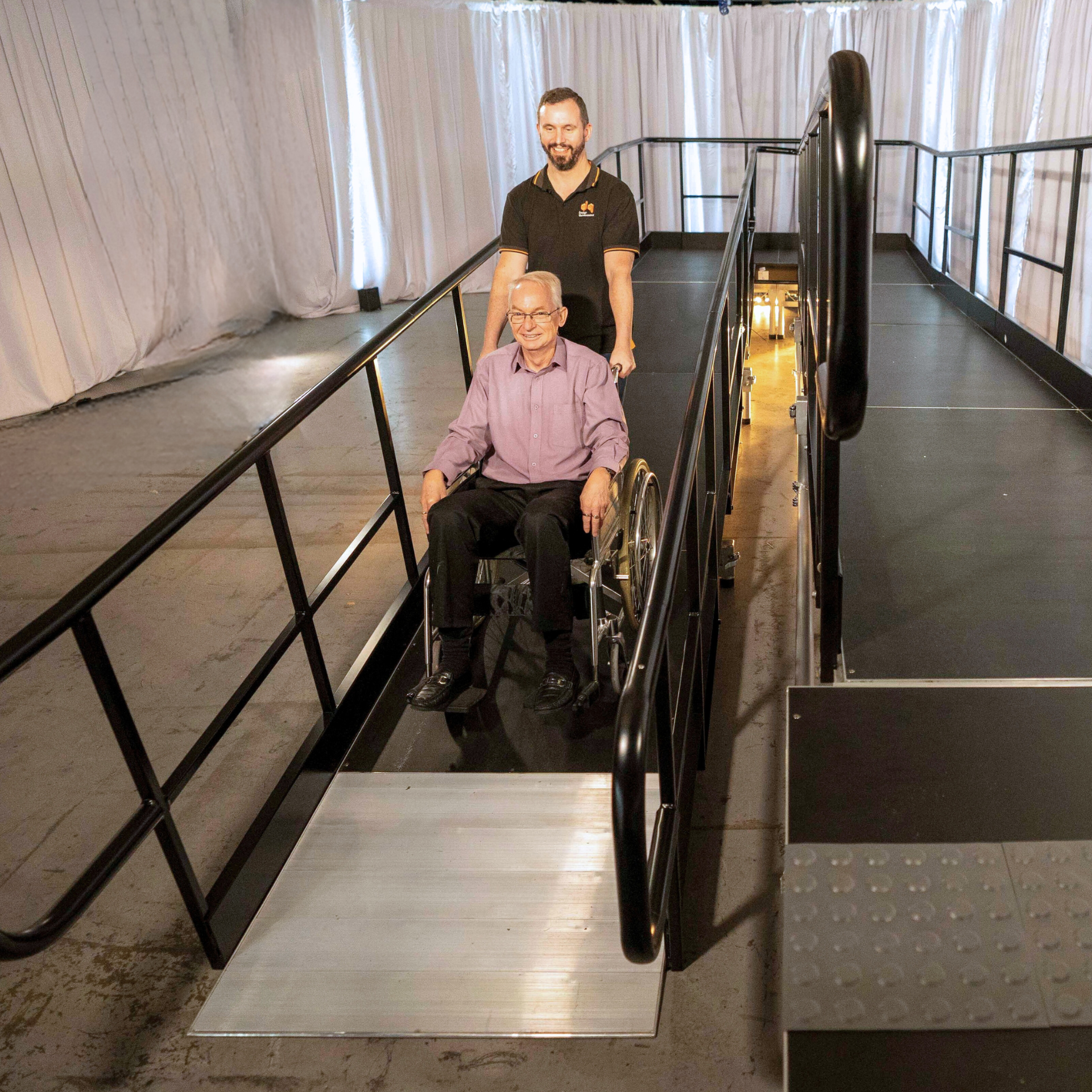 Man assisting wheelchair user down modular access ramp designed for stage and venue accessibility